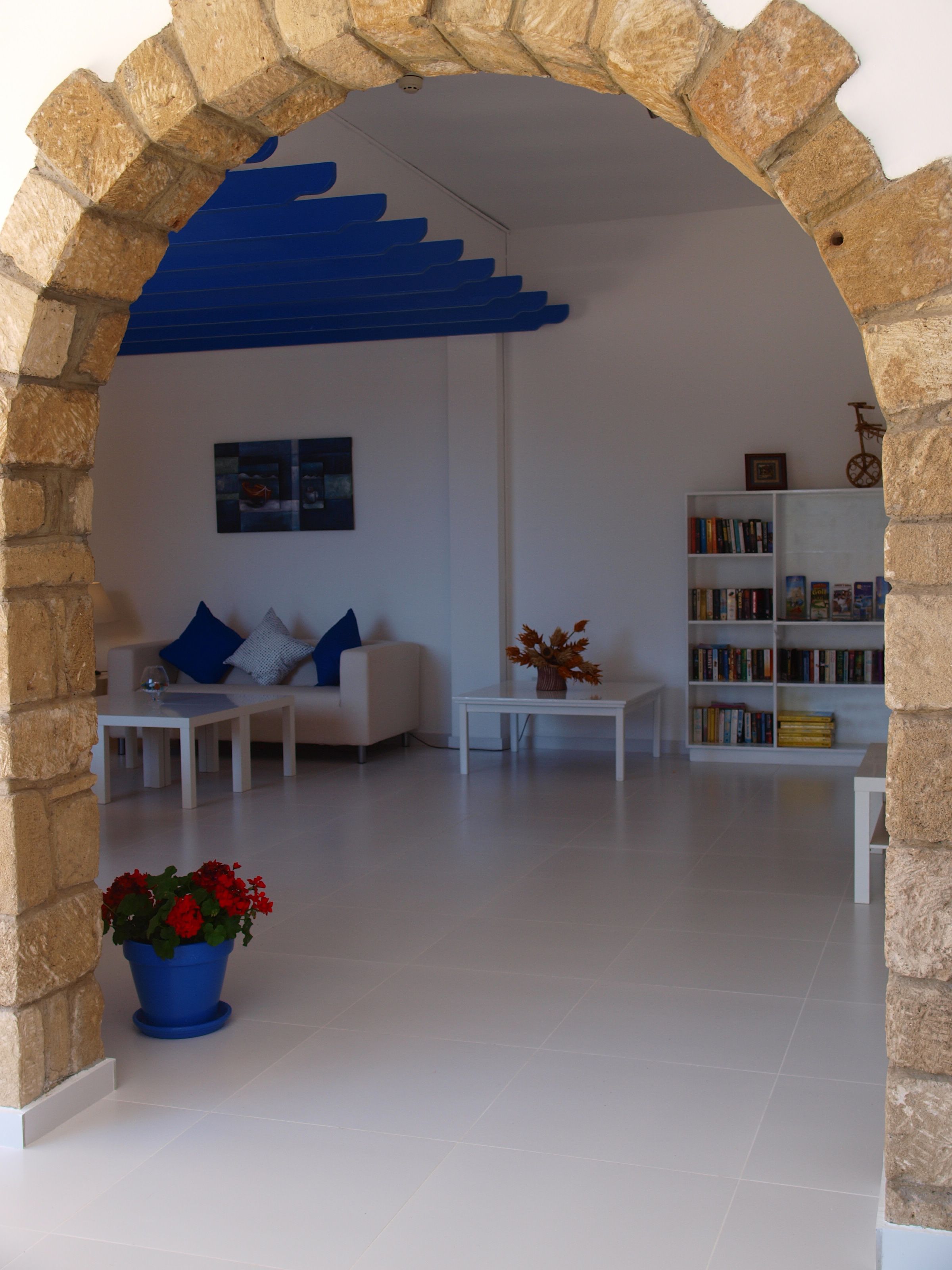 A modern living room with a stone archway, a white sofa with blue cushions, a coffee table, a bookshelf, and a potted plant.