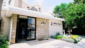 Entrada de um hotel com fachada de pedra, porta de vidro e placa com a inscrição 'Hilton Gardens Hotel Apartments'.