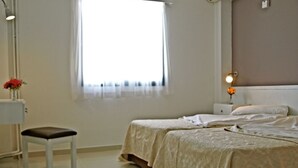 Quarto com duas camas, uma mesa de cabeceira, uma cadeira, janela com cortinas e luminária fixada na parede.