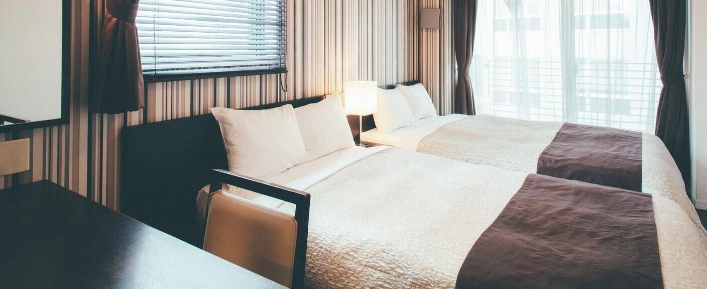Et hotelværelse med to senge, et skrivebord og en stol.