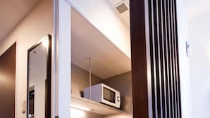 Une chambre d’hôtel moderne avec un plancher en bois foncé, une porte blanche, un four à micro-ondes intégré et une petite kitchenette équipée d’un évier et d’un plan de travail.