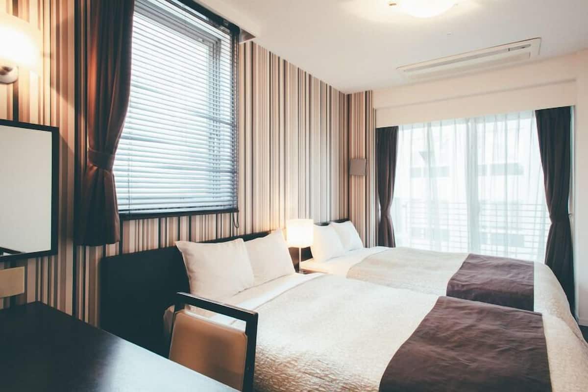 A hotel room with a bed, a desk, a chair, a lamp, and a window with curtains.