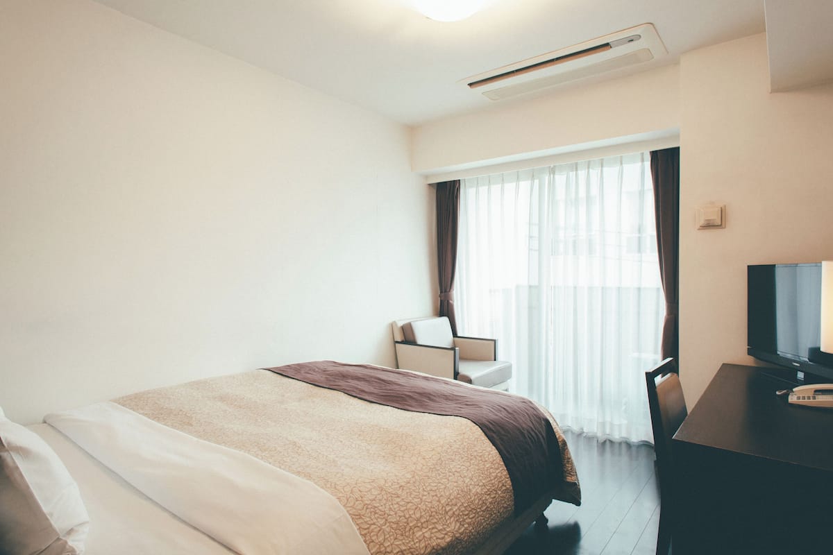 A hotel room with a bed, a desk with a television, and a chair.