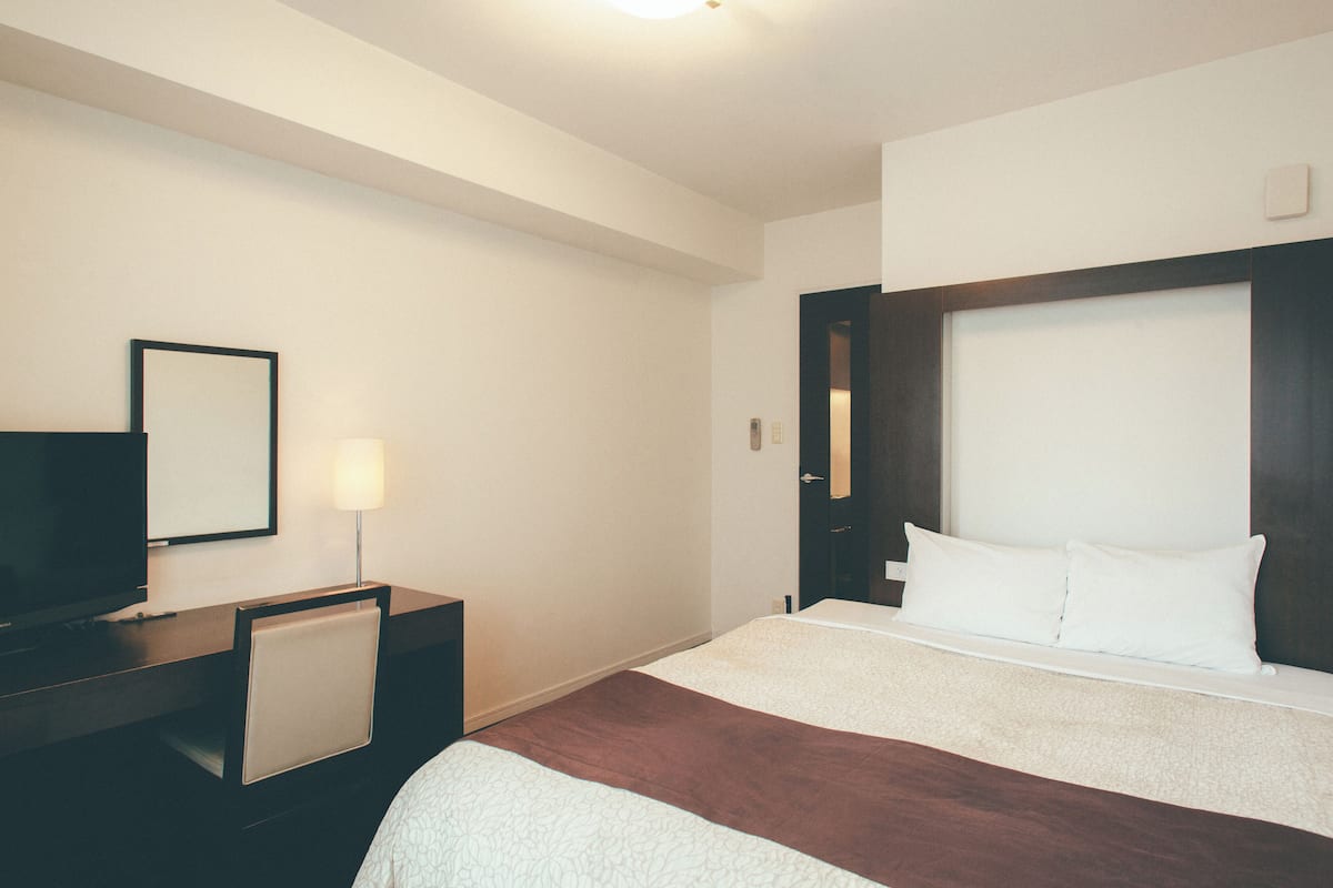 A hotel room with a bed, a desk with a chair, a television, and a nightstand.
