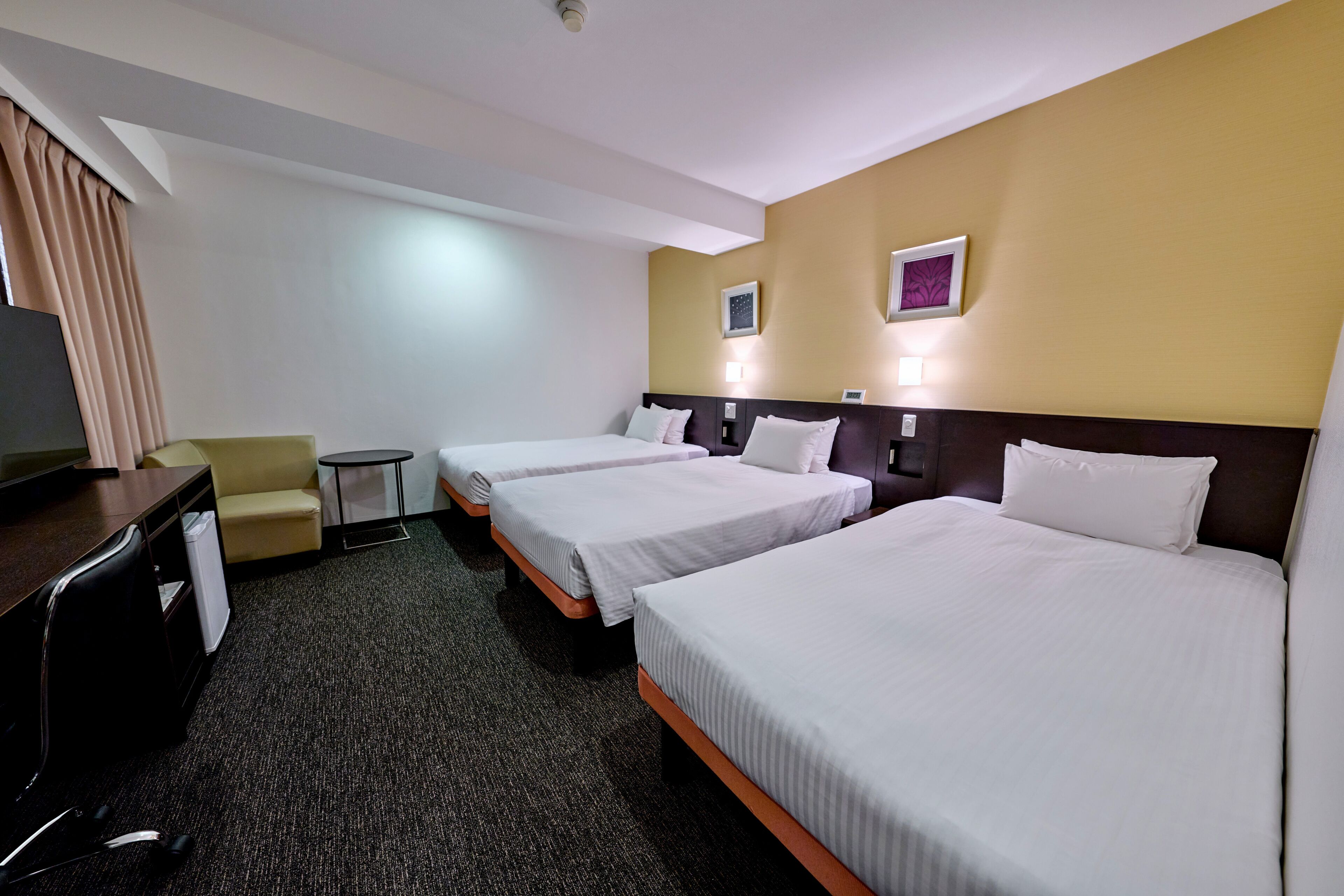 A hotel room with two beds, a desk, a chair, and a small table.