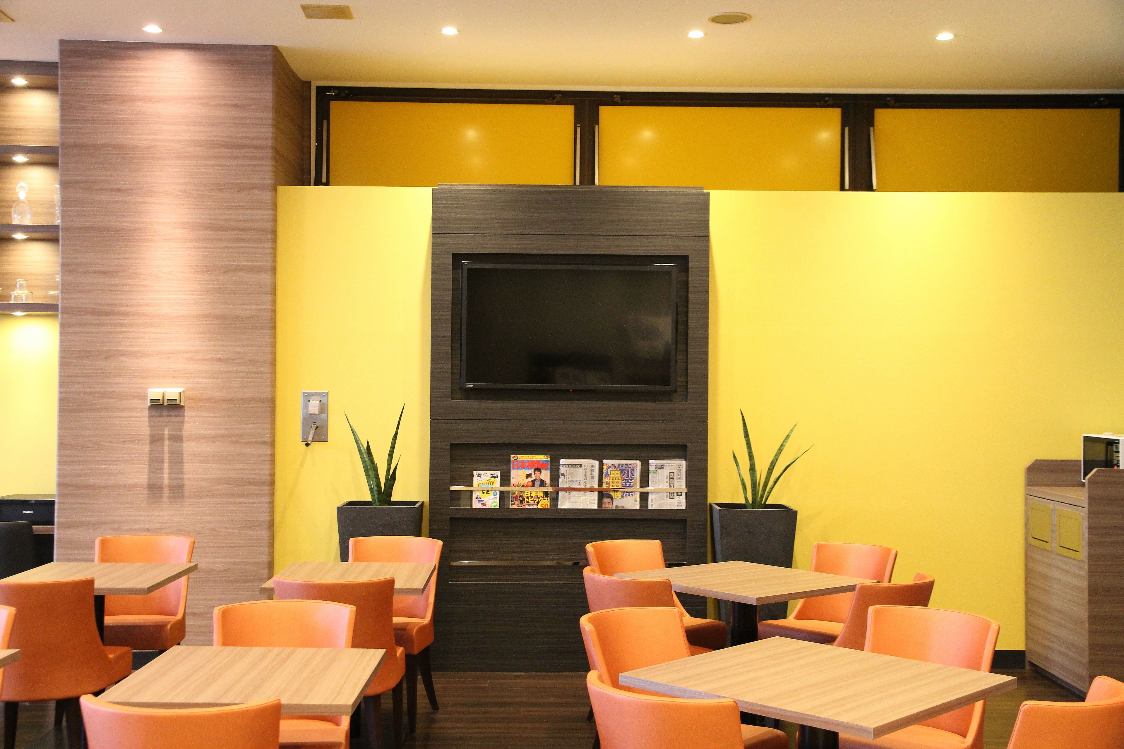 Un restaurant aux murs jaunes, aux chaises orange et doté d’un téléviseur fixé au mur.