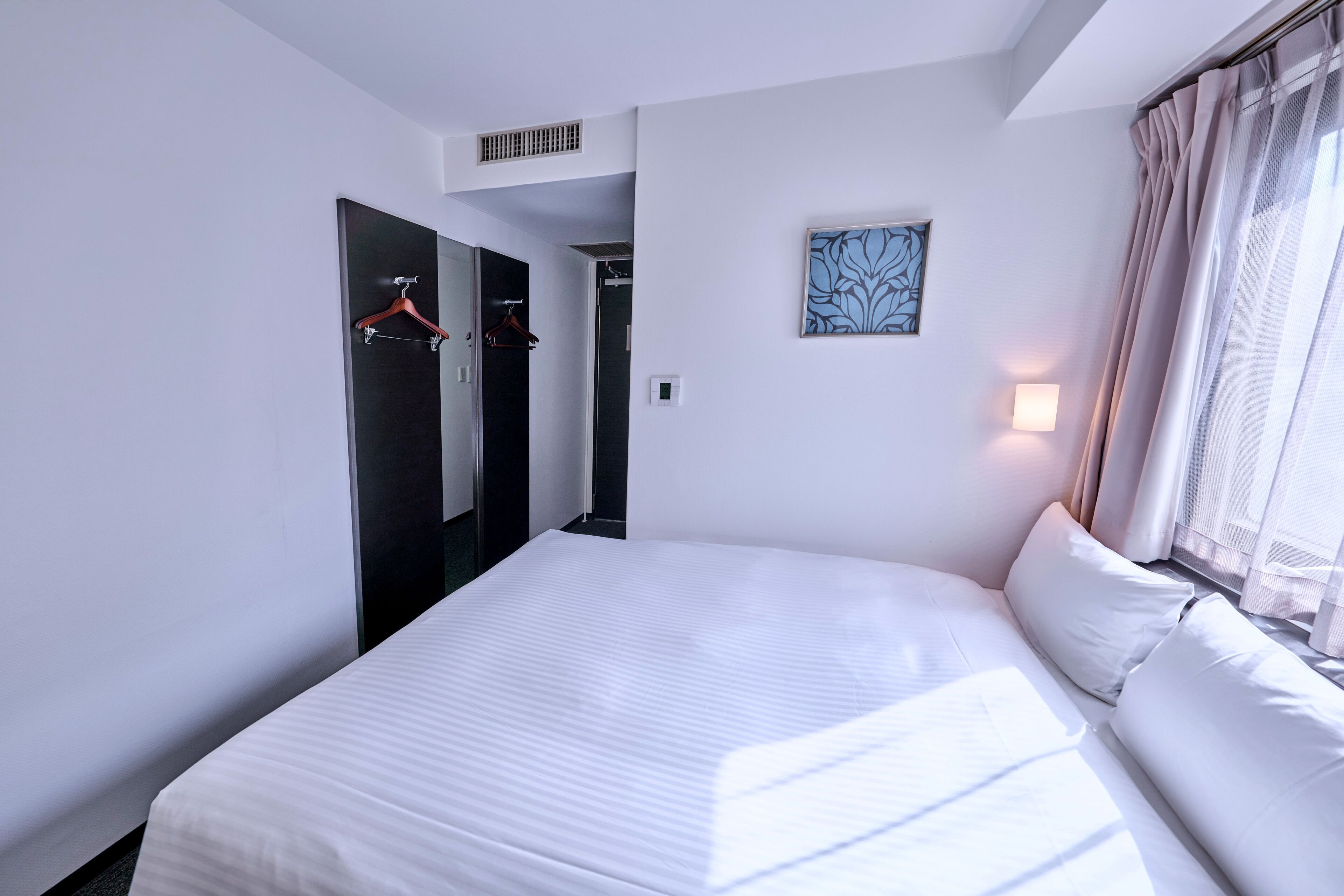 Een hotelkamer met een groot bed, een kast, een schilderij en een raam met gordijnen.
