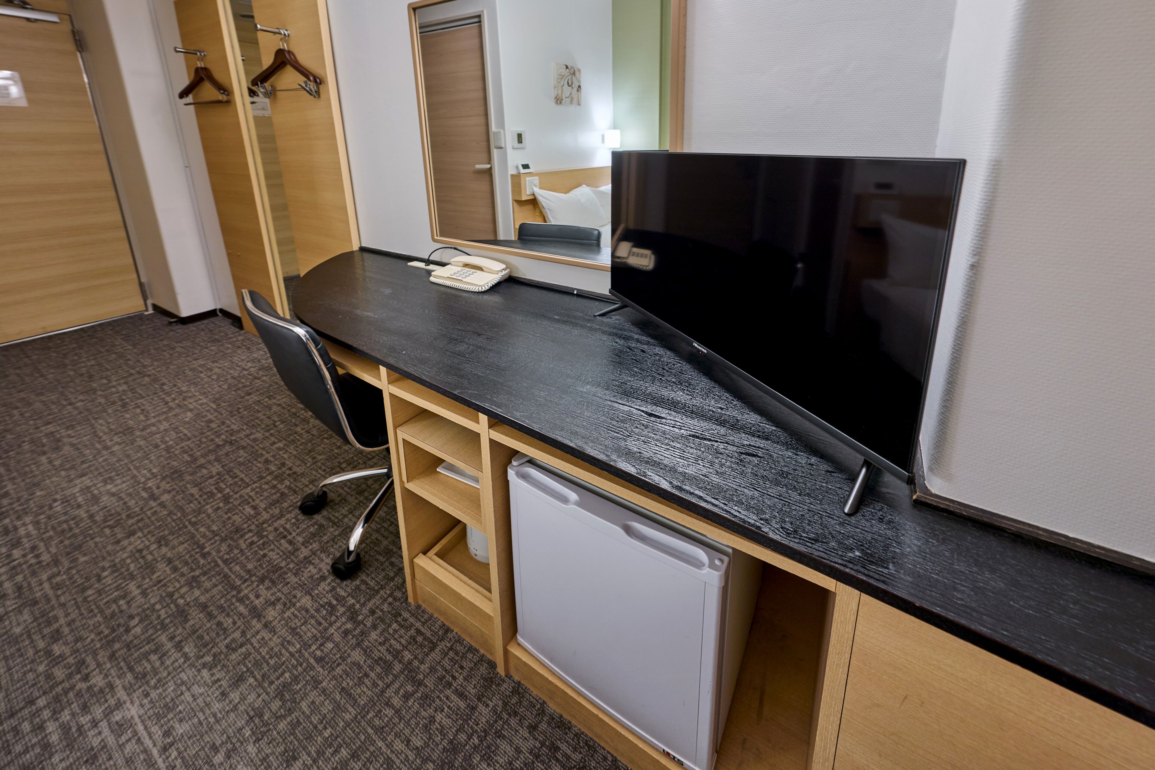 A hotel room with a desk, chair, and a small refrigerator.