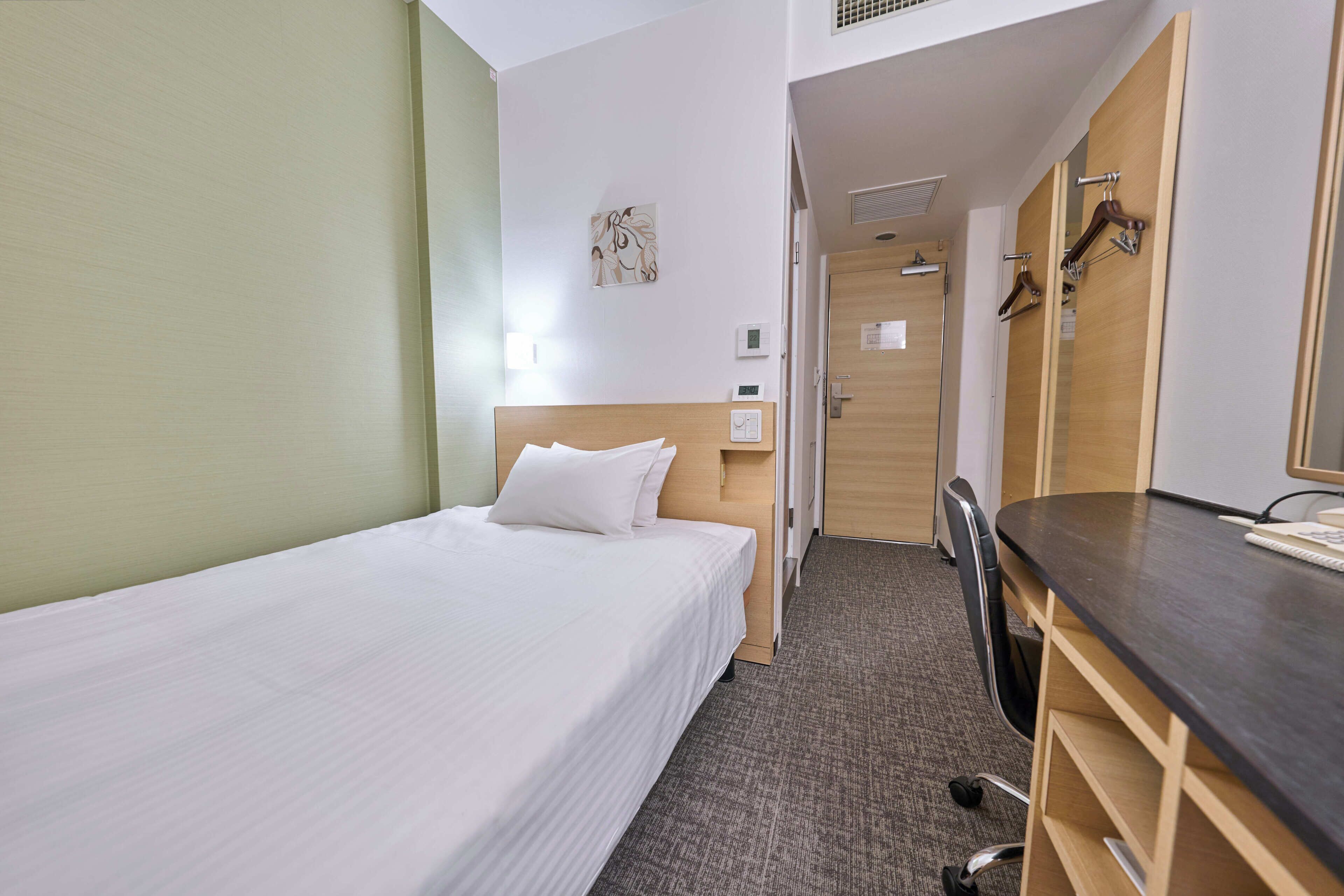 A hotel room with a single bed, a desk, a chair, and a wardrobe.