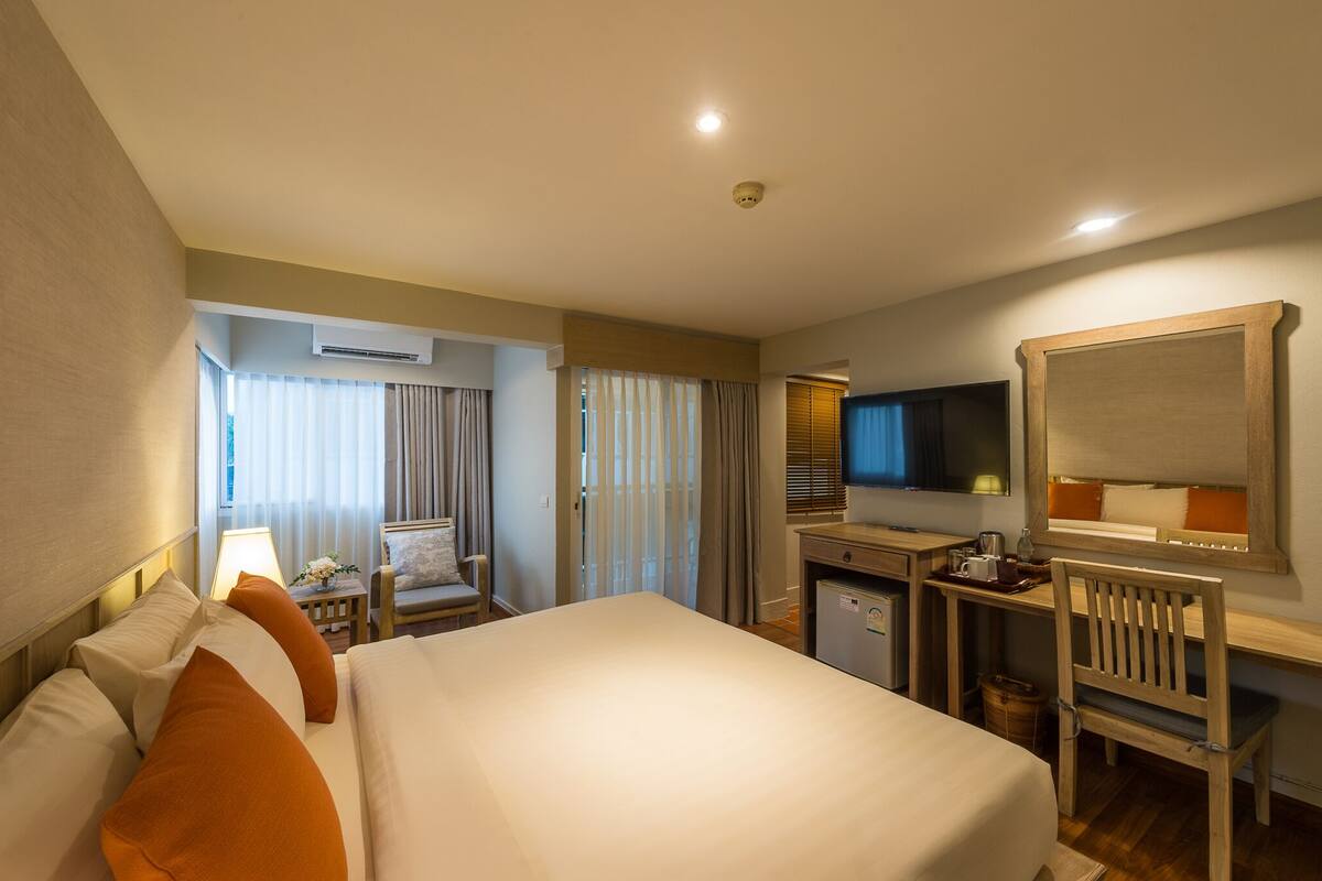 Une chambre d’hôtel avec un grand lit, un bureau avec un ordinateur, une télévision et une petite kitchenette.