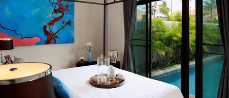 A hotel room with a bed, a drum, a painting, a tray with candles, and a view of a swimming pool.
