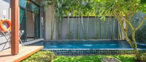 A modern outdoor pool area with a wooden deck, a lounge chair, and a stone wall with bamboo plants.
