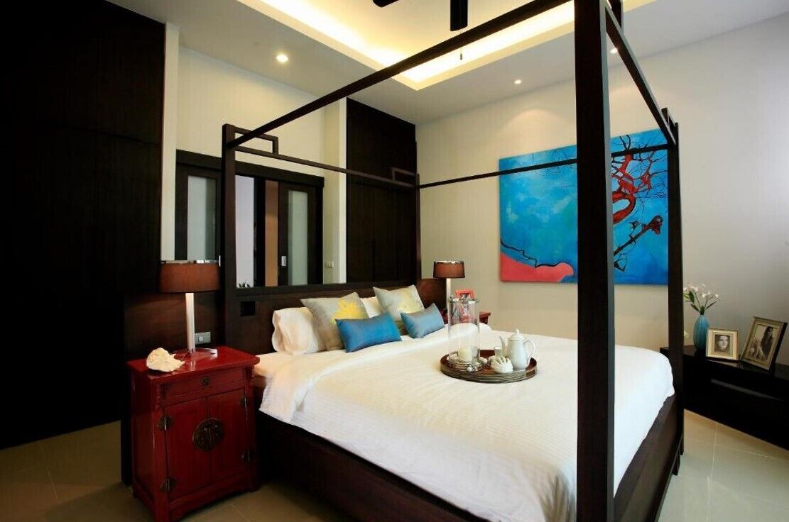 A four-poster bed with a tray of tea and cream, a red nightstand, and a large abstract painting on the wall.