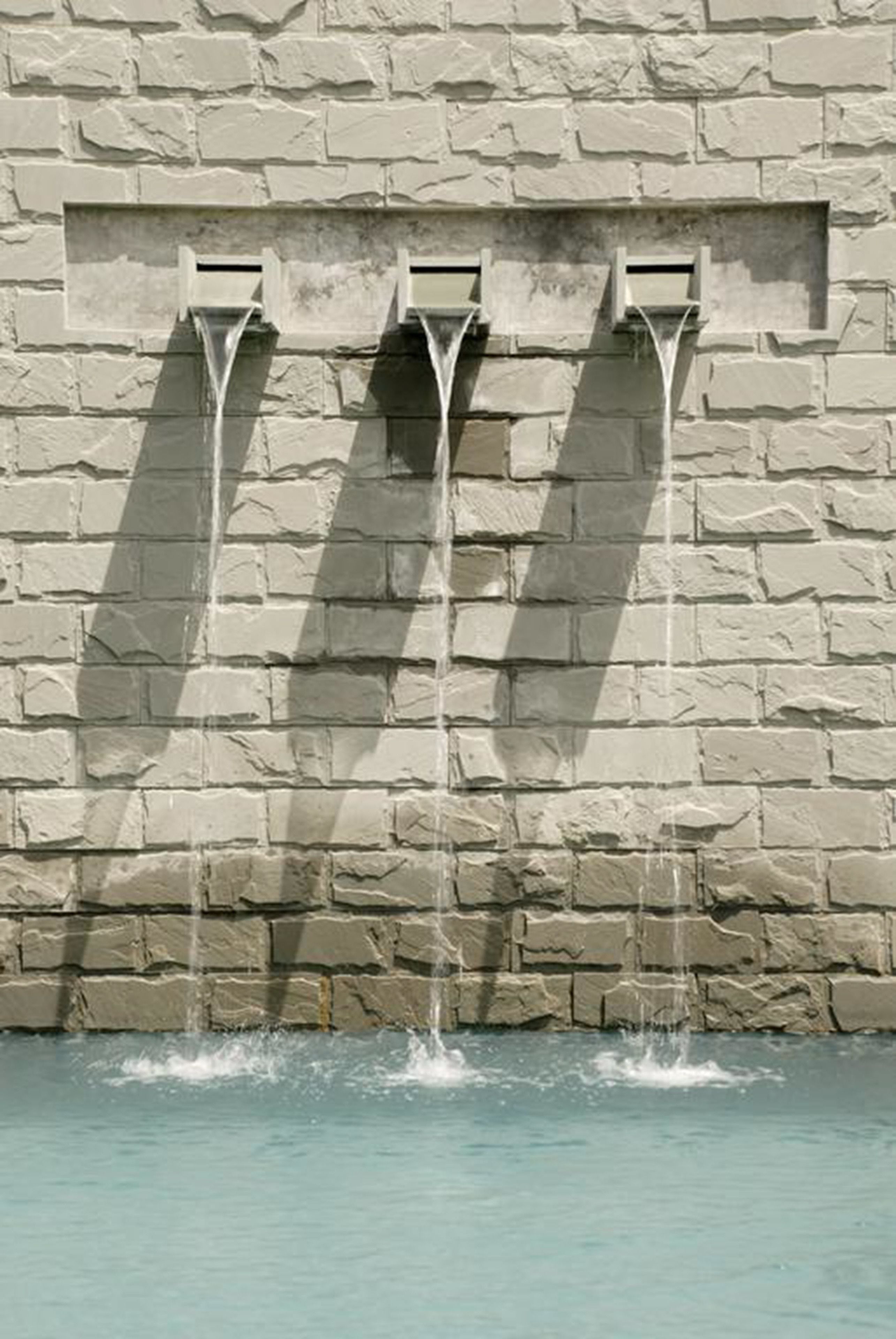 A stone wall with three water spouts.