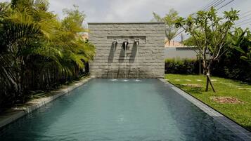 A swimming pool with a stone wall and water spouts, surrounded by lush greenery.