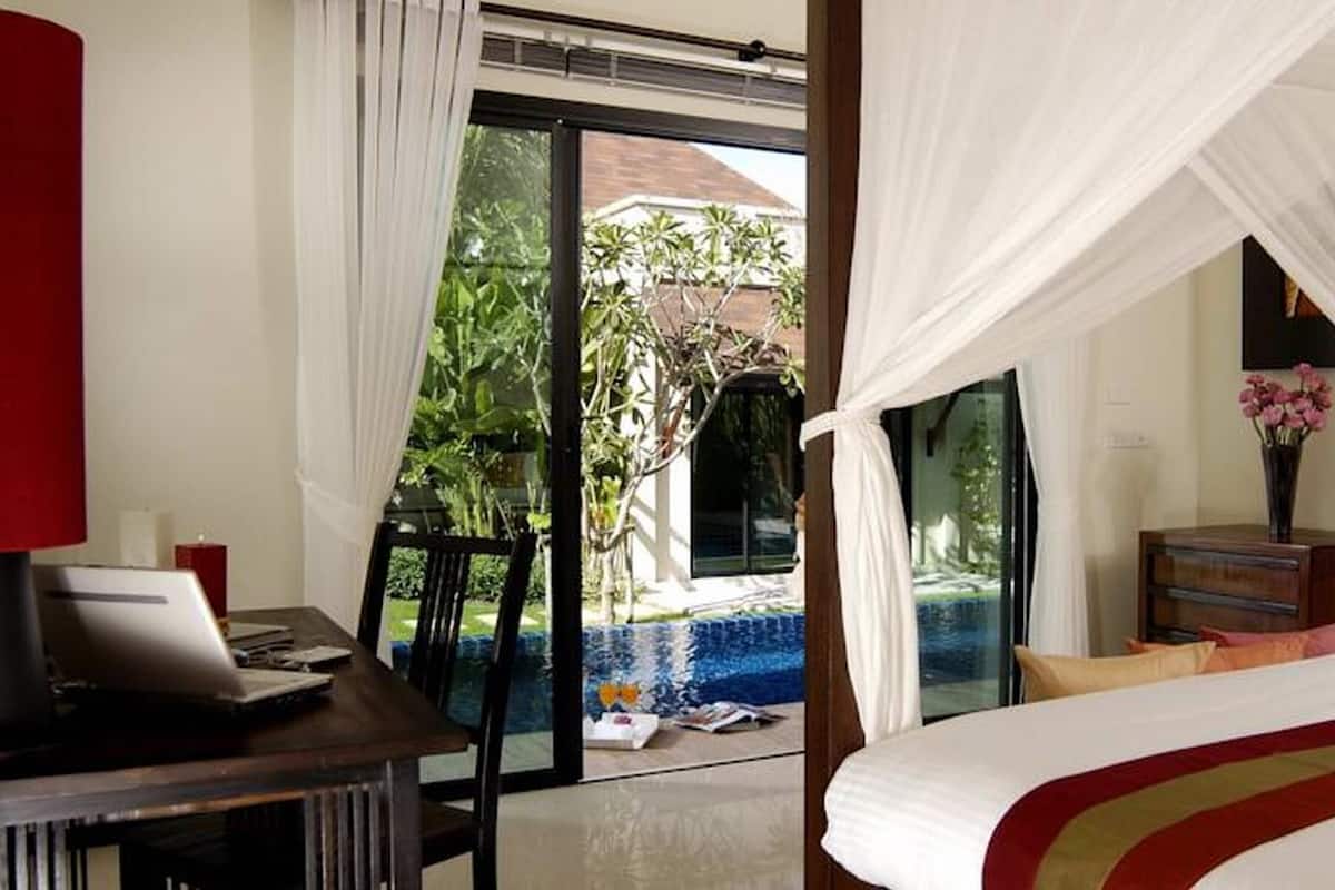 Habitación de hotel con cama, escritorio con una computadora portátil, cómoda de madera y vista a un área de piscina al aire libre.