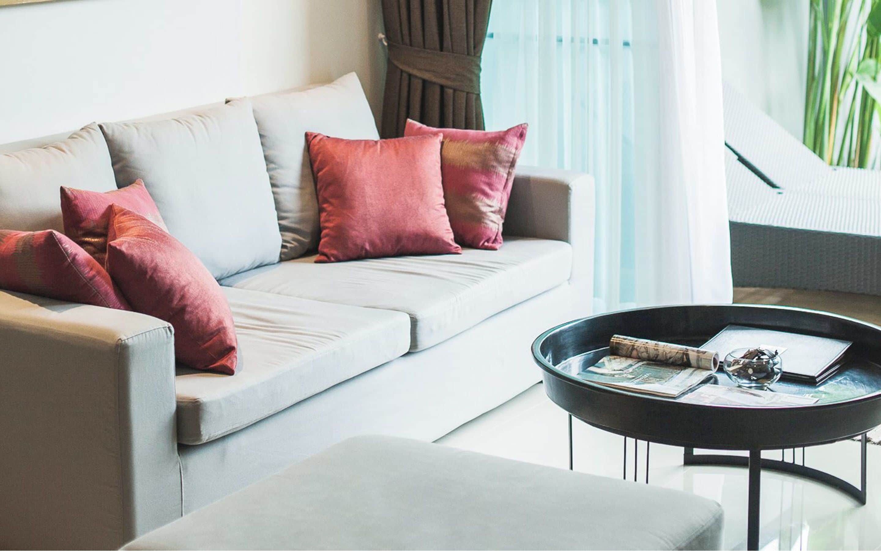 A modern living room with a sofa, cushions, and a glass coffee table with books and a decorative item.