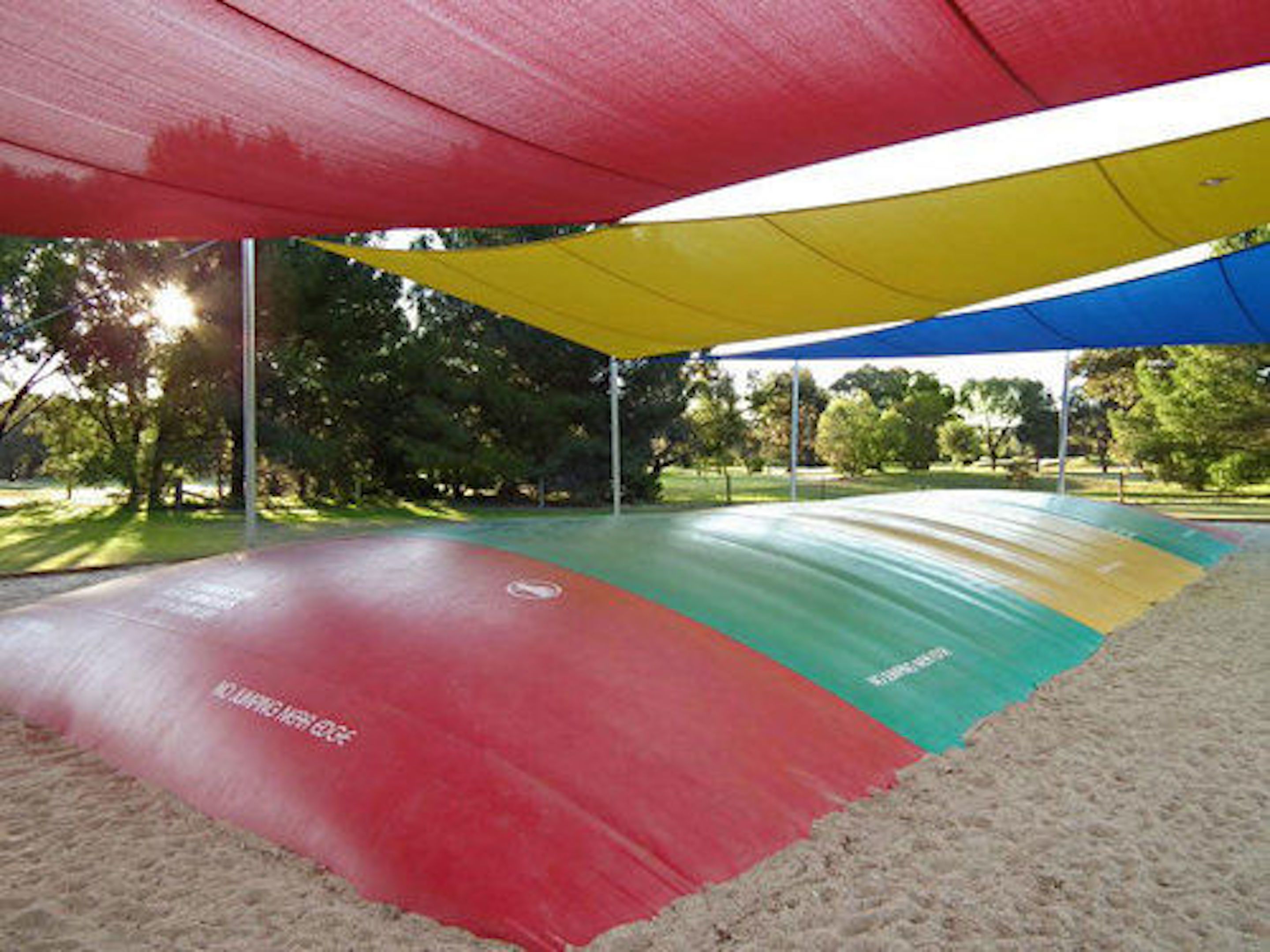 A covered outdoor area with a colorful floor, surrounded by trees and a grassy field.