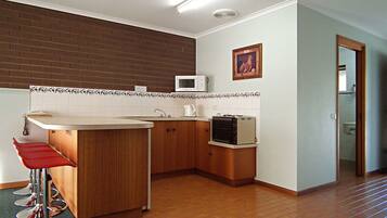 Una cocina compacta con microondas, tostador y pileta. Se observan muebles de madera y un taburete rojo.