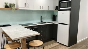 A modern kitchen with a marble countertop, black cabinets, a white refrigerator, and a built-in microwave. - Cobram Barooga Golf Resort (Barooga)