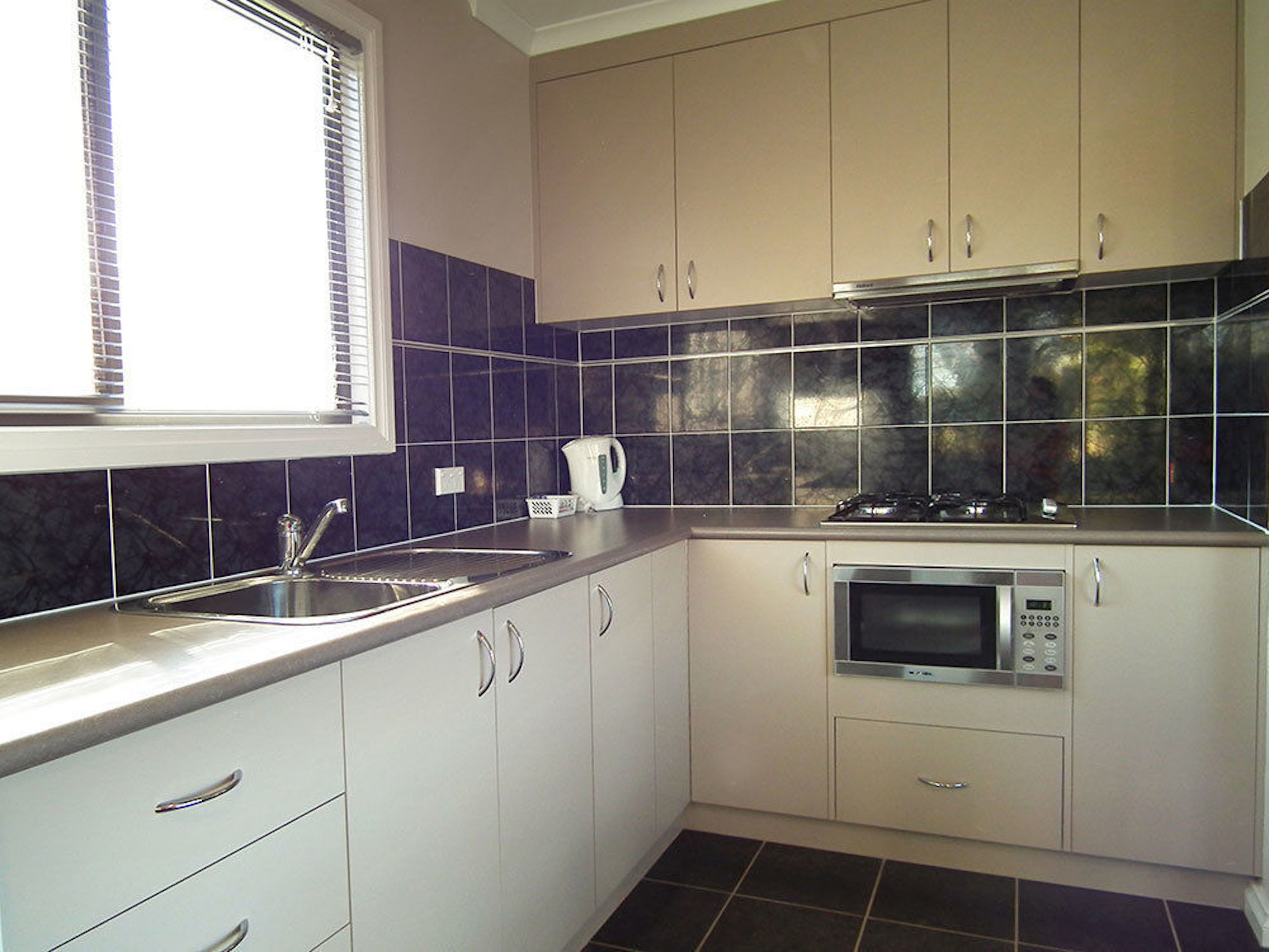 A kitchen with white cabinets, a stainless steel sink, a microwave, and a stove.