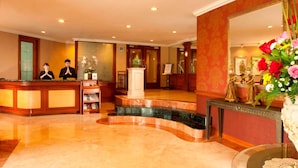 Zona de recepción de un hotel con suelo de mármol, mostrador de recepción, un espejo grande y una estatua.