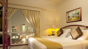 Una habitación de hotel con una cama grande, una mesita de noche, una lámpara, un cuadro en la pared y vistas de la ciudad por la noche.