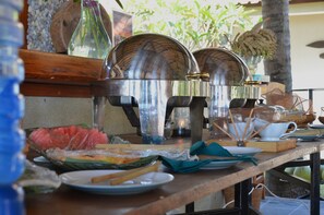 Una mesa con alimentos, incluyendo sandía envuelta y una cesta de verduras, además de una vela.