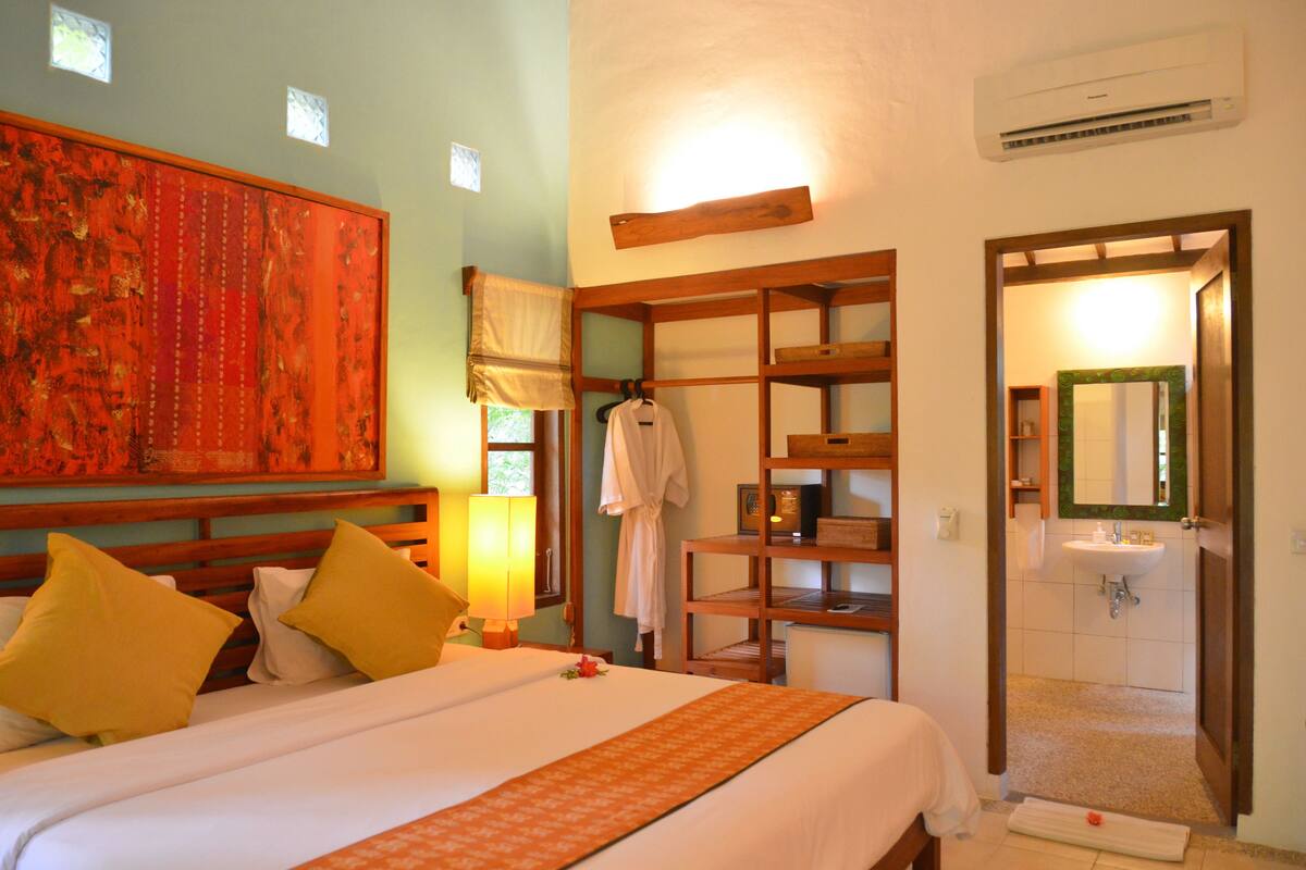 A hotel room with a large bed, a wardrobe, a bathroom with a sink, and a large painting on the wall.