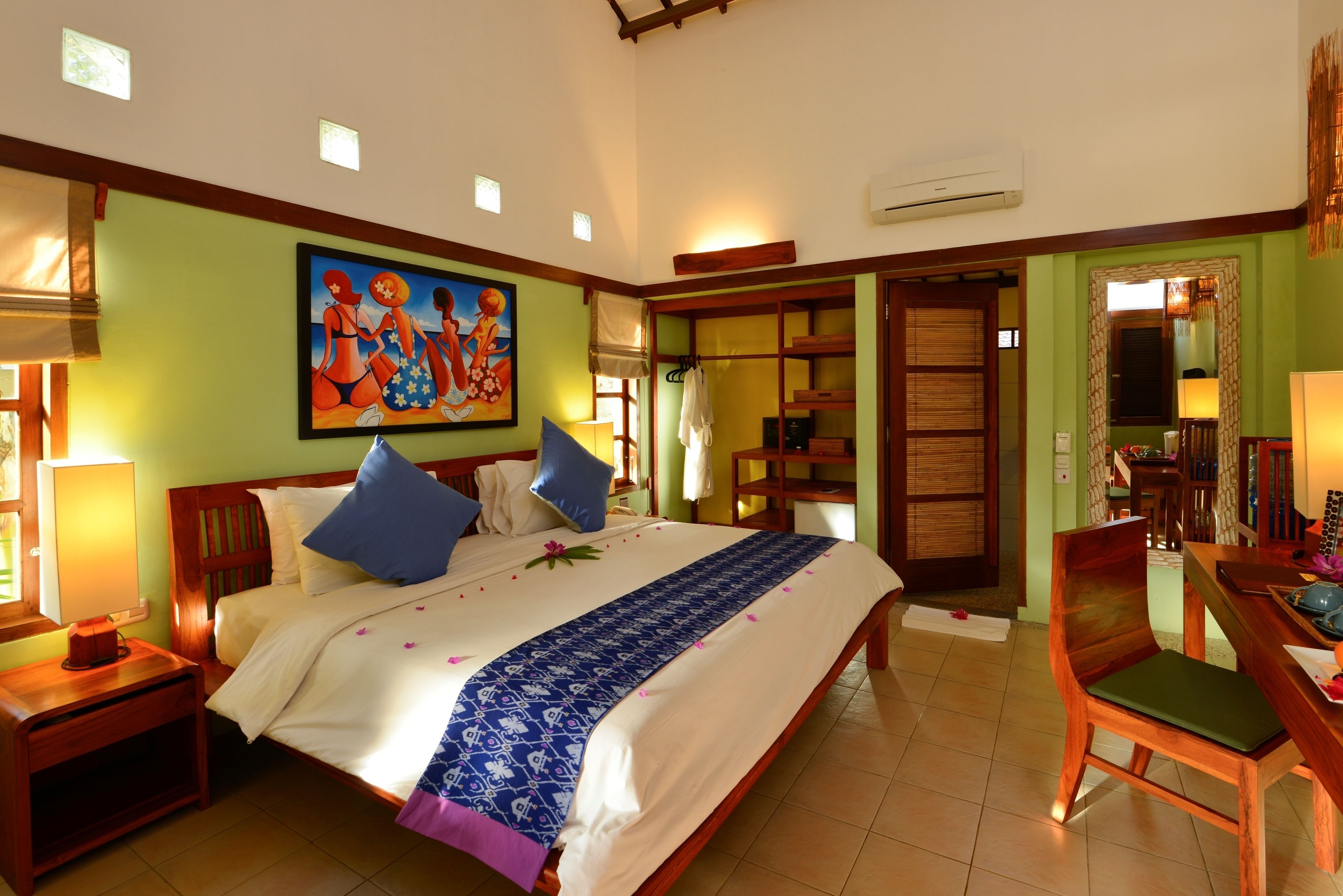 A hotel room with a large bed, a desk, and a chair. There is a painting on the wall and a window with blinds.