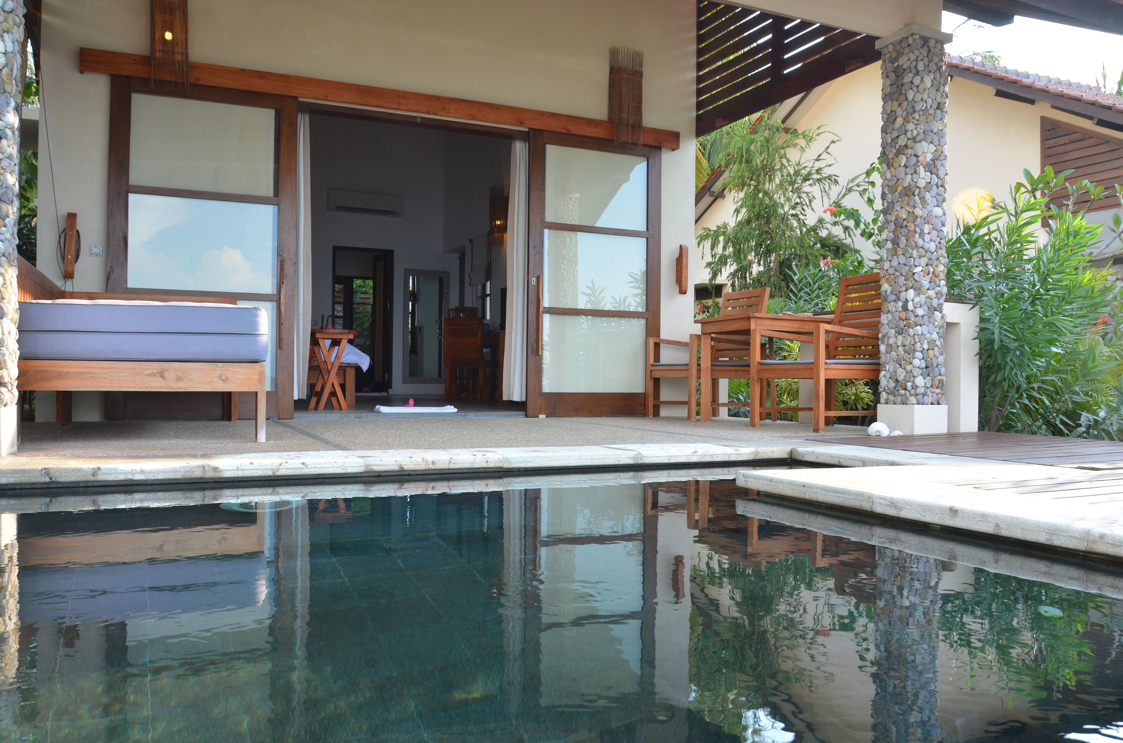 Un área junto a la piscina con un banco, sillas de madera y un pilar de piedra.