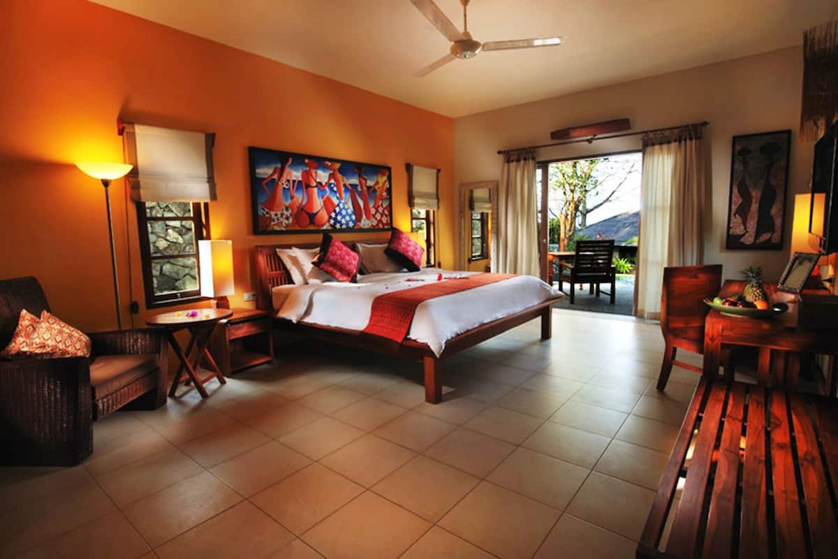 A spacious bedroom with a large bed, a sitting area with a table and chairs, a ceiling fan, and a view of the outdoors through a window.