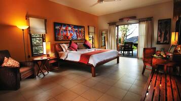 A spacious bedroom with a large bed, a sitting area with a table and chairs, a ceiling fan, and a view of the outdoors through a window.