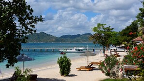 A beach with lounge chairs, umbrellas, and a boat docked near the shore. - Cocotinos Sekotong, a Boutique Beach Resort & Spa (Sekotong Barat)