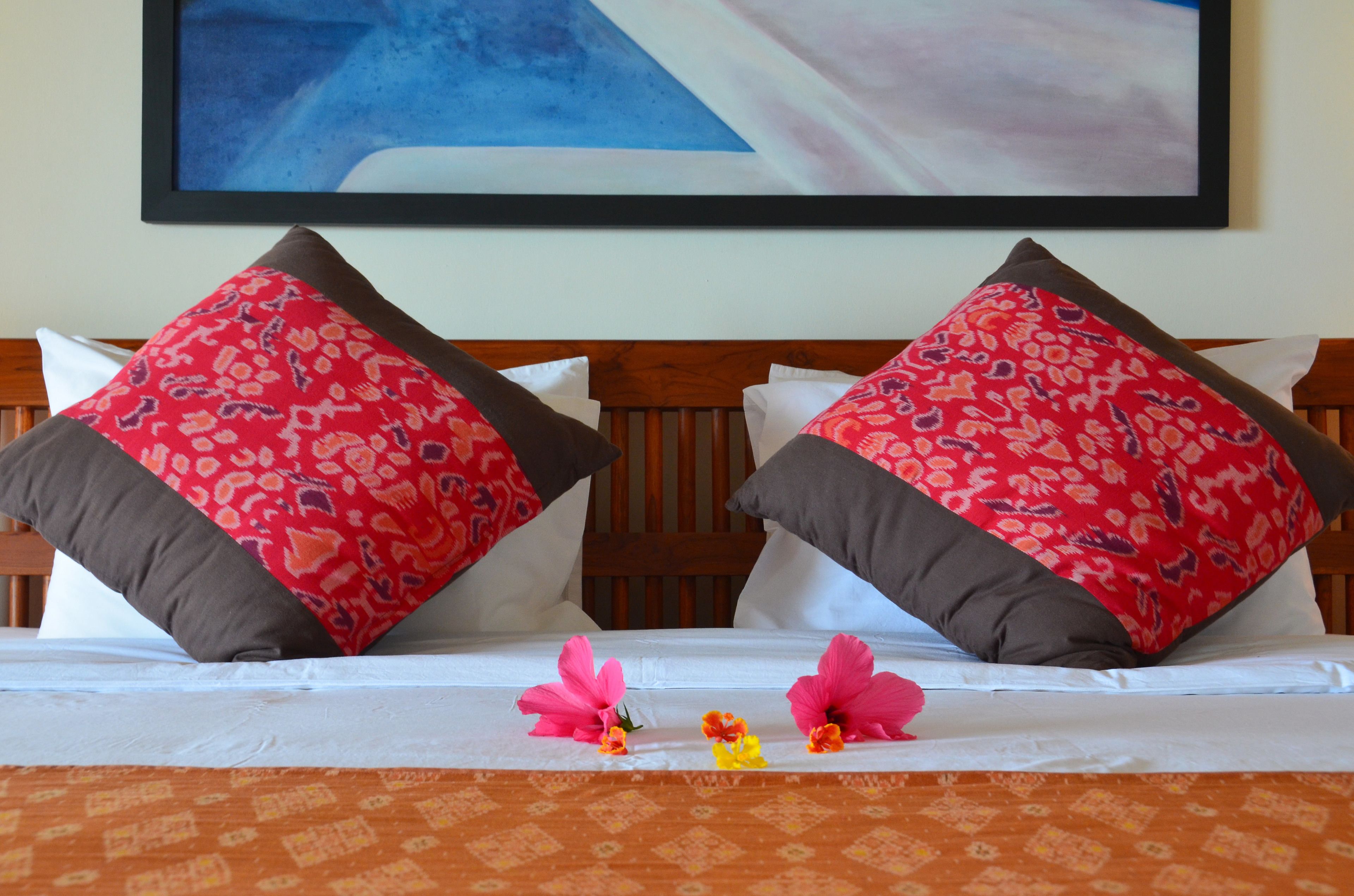 A bed with two red patterned pillows, a white pillow, and a wooden headboard.