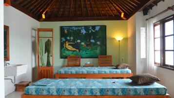 Une pièce avec deux lits en bois, un tableau représentant un paysage tropical, un lavabo et une fenêtre avec des rideaux.