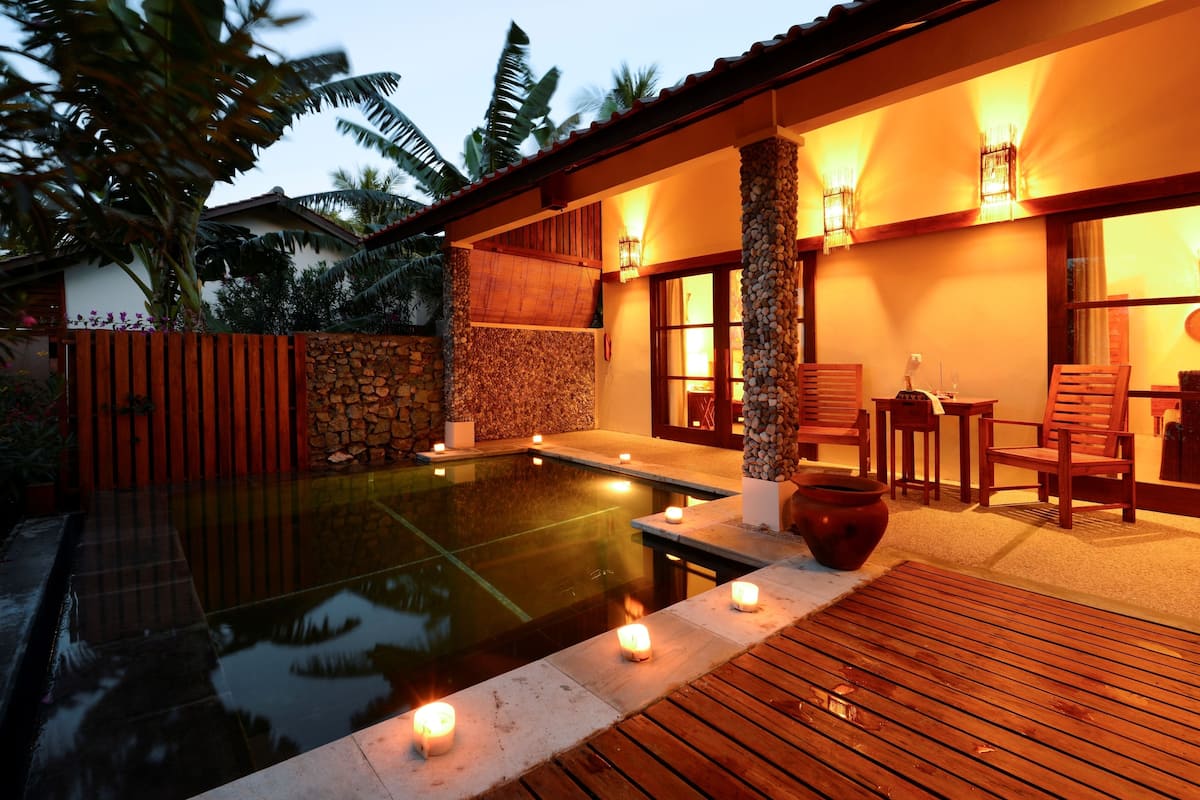 A poolside area with a wooden deck, stone walls, and a seating arrangement with chairs and tables.