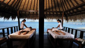 A wooden deck with two beds, each with a person lying down, overlooking a beach and ocean. - Cocotinos Sekotong, a Boutique Beach Resort & Spa (Sekotong Barat)