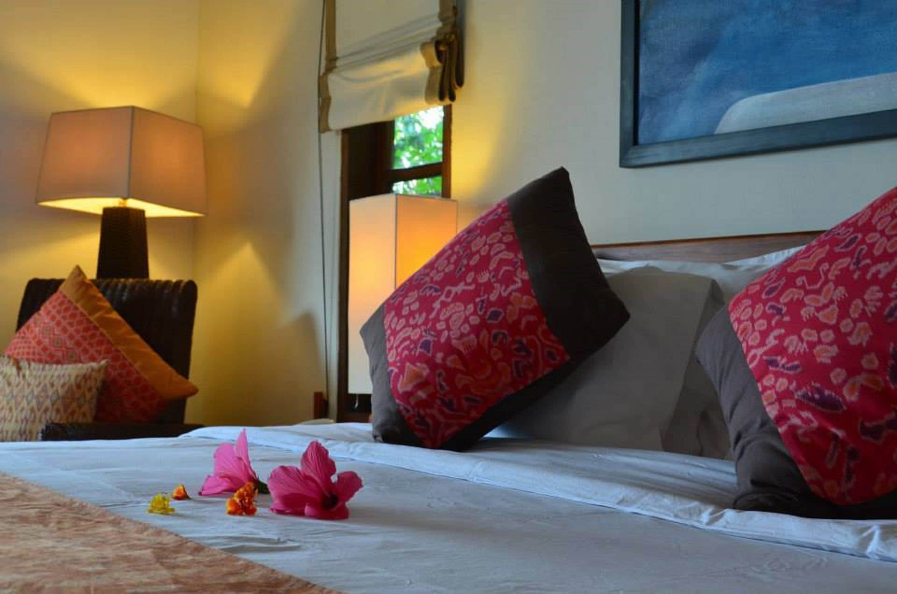Una habitación de hotel con una cama, almohadas, una lámpara y un cuadro en la pared.