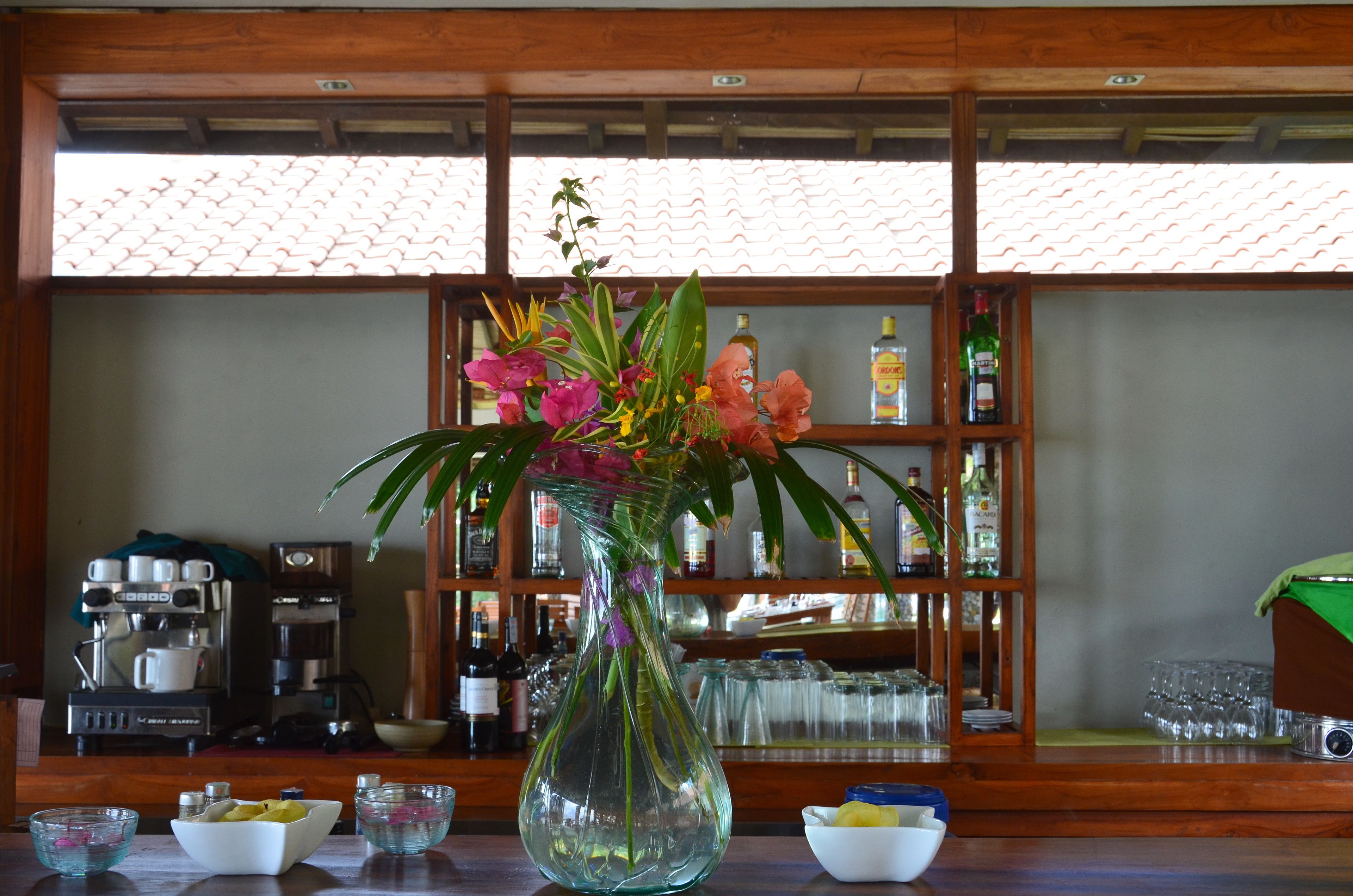 A bar area with a clear glass vase of flowers, a coffee machine, and shelves with bottles and glasses.