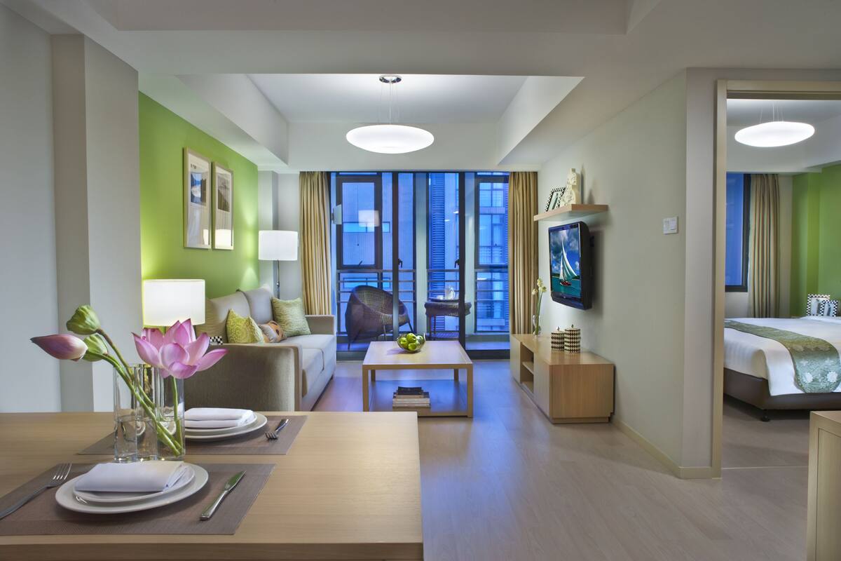 A hotel room with a dining area, a sofa, a television, and a bed.