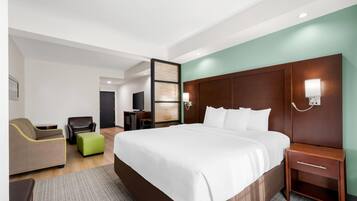 A hotel room with a large bed, a desk, a chair, a television, and a wall-mounted light.