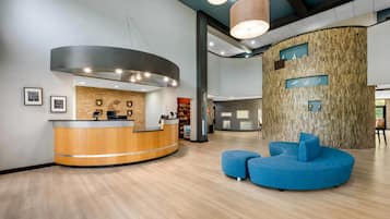 Zona de recepción con un mostrador de madera curvado, un área de asientos azules y una pared con diseño de paneles de madera.