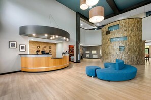 Een receptiebalie van hout met een gebogen vorm, een blauwe zithoek en een wand met houten paneeldecoratie.