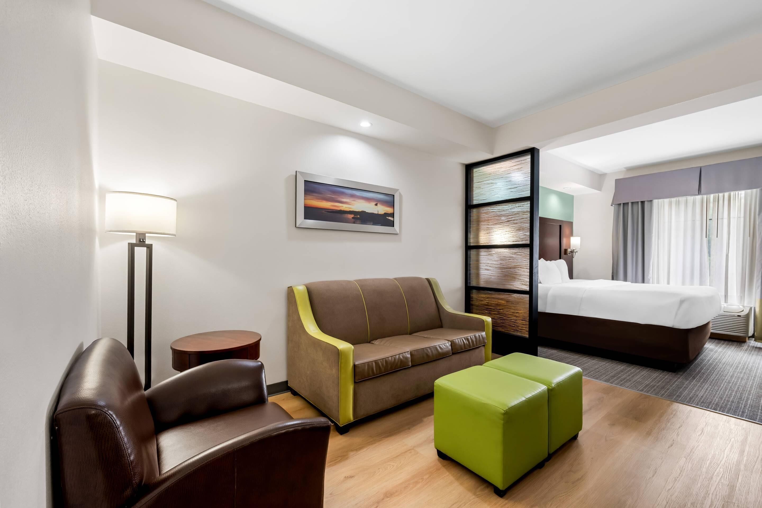 A hotel room with a bed, a sofa, a chair, a small table, and a lamp.