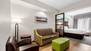 A hotel room with a bed, a sofa, a chair, a small table, and a lamp.