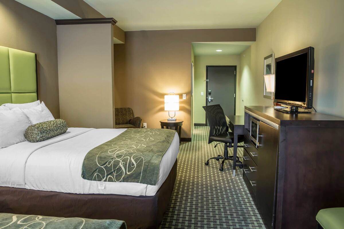 Une chambre d’hôtel avec un lit, un bureau avec un ordinateur, une télévision et une lampe.