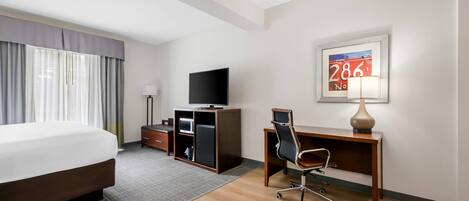 A hotel room with a bed, desk, chair, television, and a framed picture on the wall.