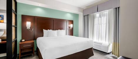 A hotel room with a large bed, a nightstand, a lamp, a wall-mounted TV, and a window with curtains.
