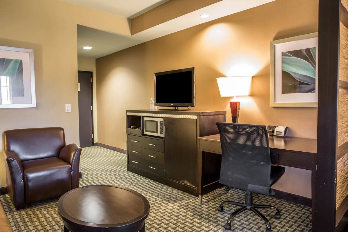 Une chambre d’hôtel avec un fauteuil en cuir marron, un bureau avec un ordinateur, un téléviseur à écran plat, un four à micro-ondes, une lampe et un tableau encadré au mur.